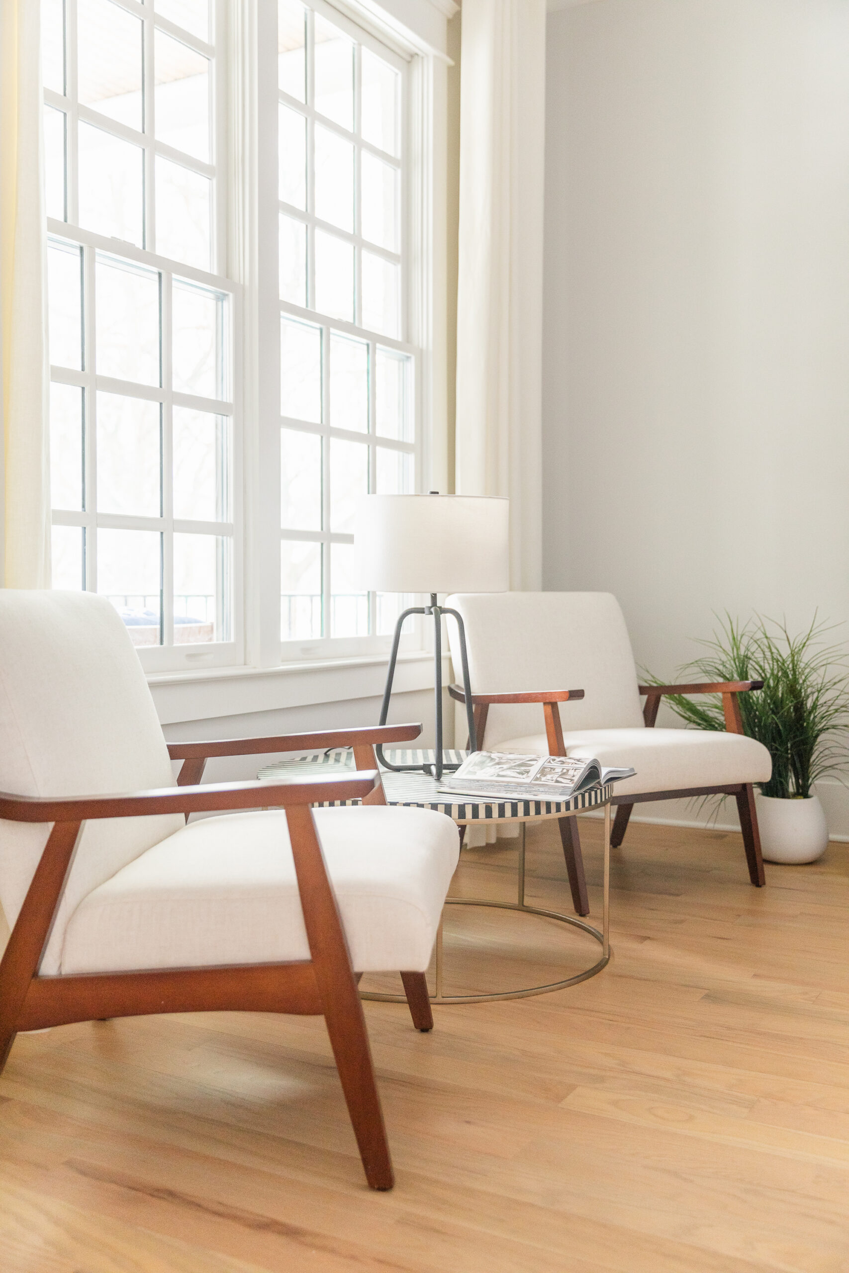Bright, modern sitting area with white armchairs, natural wood accents, and large windows—showcasing a clean, staged interior that adds value when selling a home.